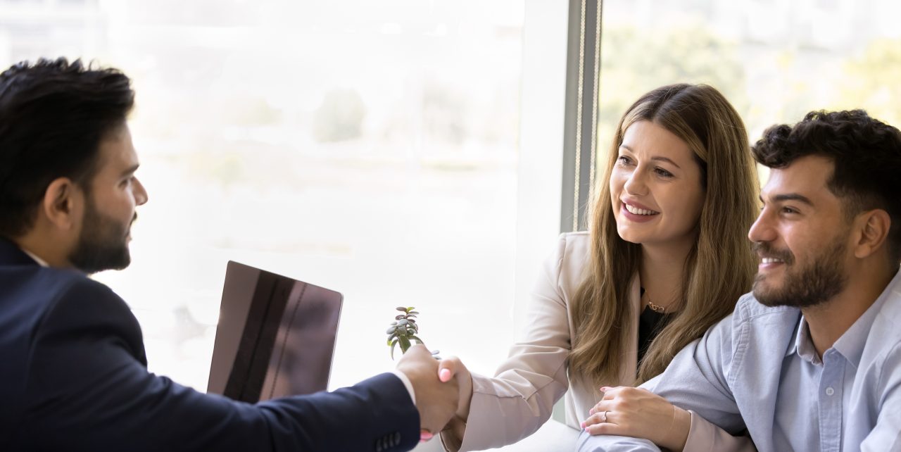 Cheerful couple of clients shaking hands with Indian lawyer man