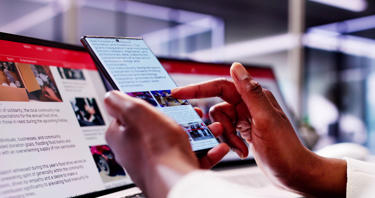 African American Woman Reading Online News on Smartphone and Laptop: Keeping Up with the Latest Headlines on the Go.