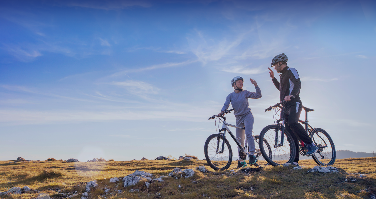 happy couple goes on a mountain asphalt road in the woods on bikes with helmets giving each other a high five